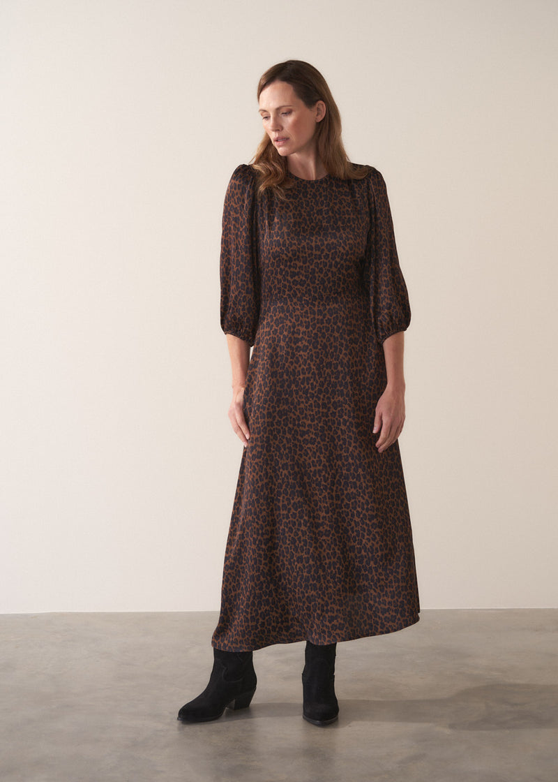 Woman wearing a leopard print satin midi dress against a plain background