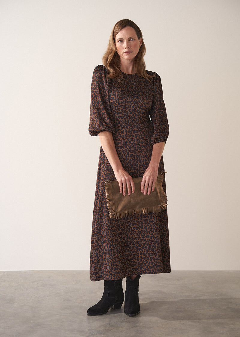 Woman wearing a leopard print satin midi dress holding a brown clutch against a plain background