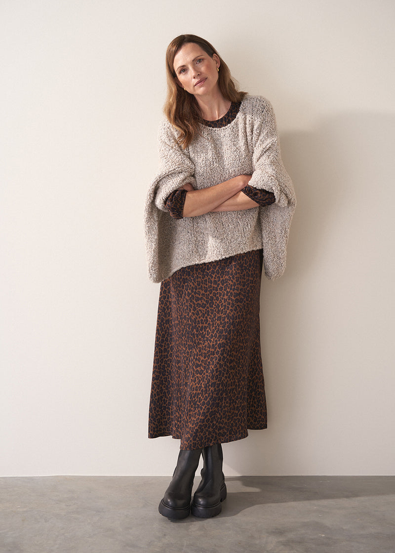Woman wearing a patterned sweater and leopard print skirt against a white wall.