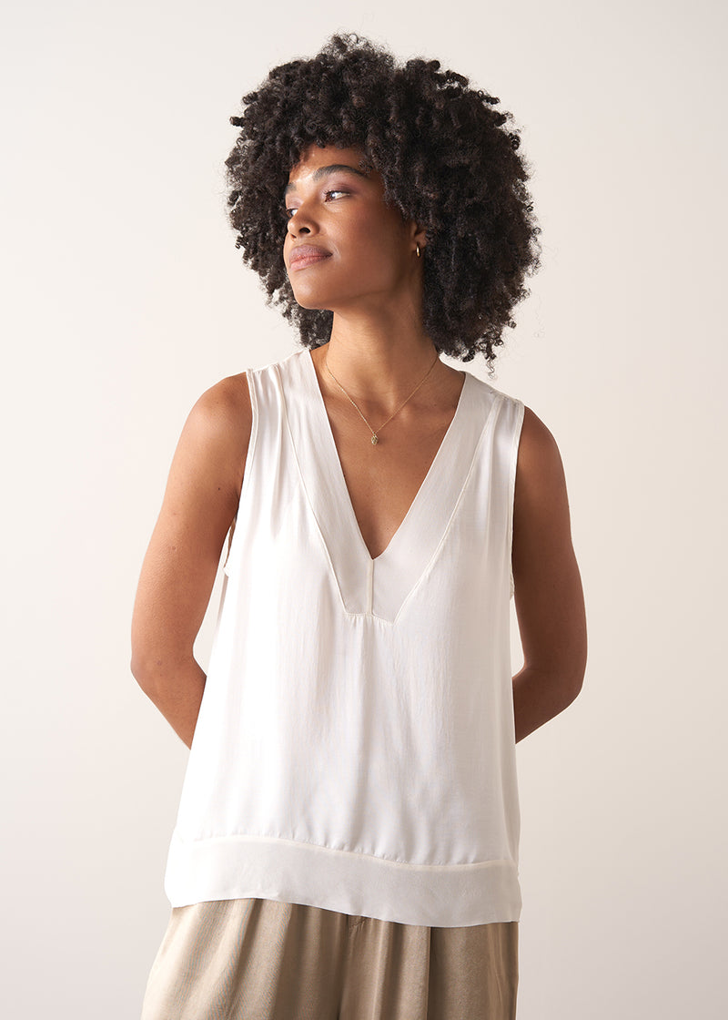 Woman wearing a white sleeveless top against a plain background