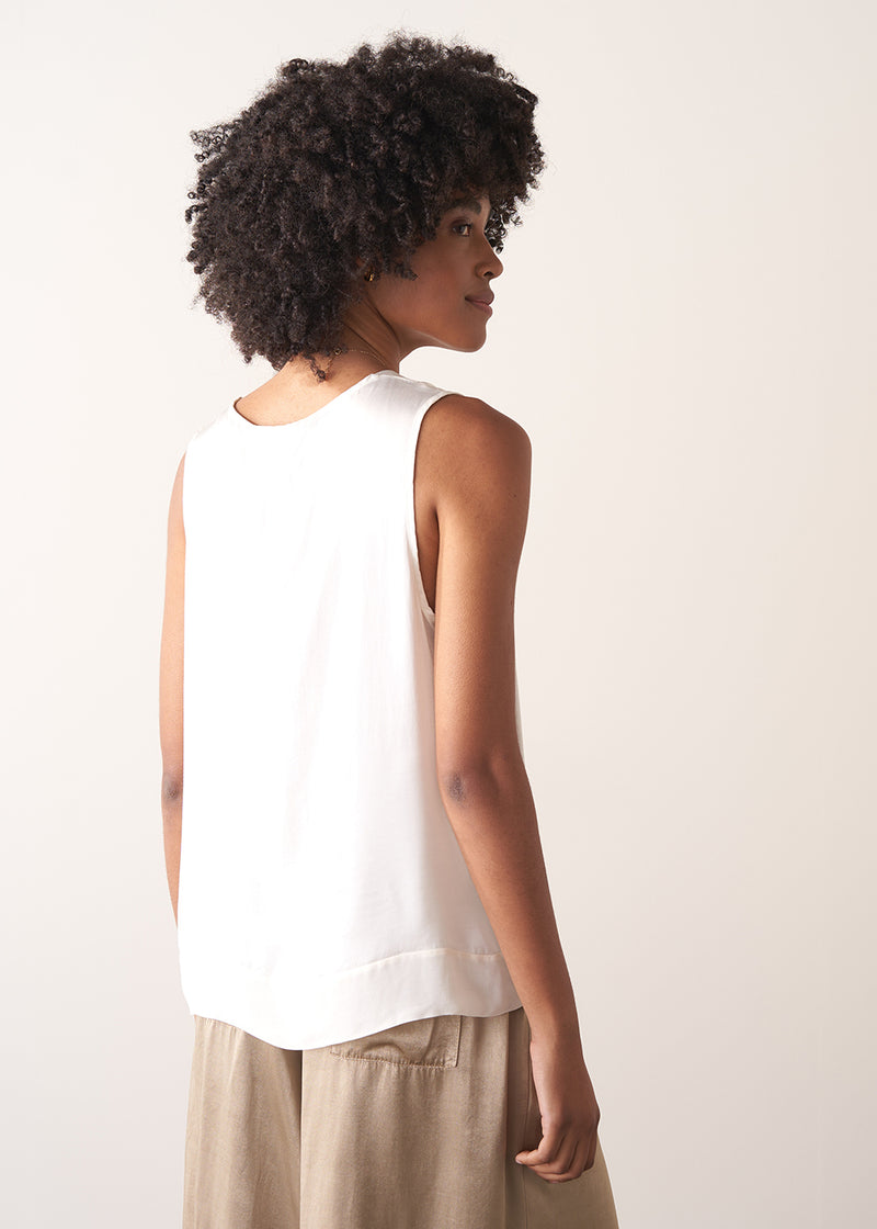 Woman wearing a white sleeveless top against a plain background