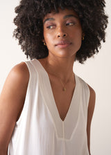 Woman wearing a white sleeveless top against a plain background