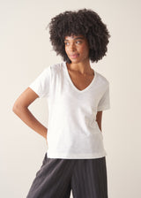 A woman wearing a white short-sleeve v-neck t-shirt and dark grey wide-leg trousers.