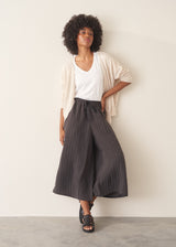 A woman wearing a white short-sleeve v-neck t-shirt and dark grey wide-leg trousers.