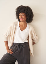 A woman wearing a white short-sleeve v-neck t-shirt and dark grey wide-leg trousers.