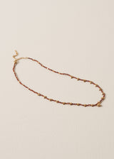 Necklace with plum crystal beads, gold discs, and a hammered heart pendant, on a beige background