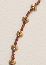 Close up of necklace with plum crystal beads, gold discs on a beige background