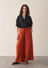 Woman wearing black broderie anglaise top and full length, wide leg red linen trousers