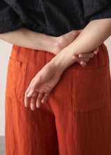 Woman wearing black broderie anglaise top and full length, wide leg red linen trousers