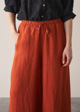 Woman wearing black broderie anglaise top and full length, wide leg red linen trousers