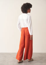 Woman wearing bright red wide leg linen trousers and white v-neck top