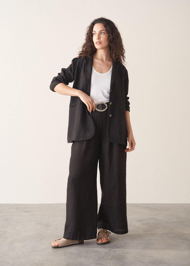 Woman wearing a black linen blazer, black wide leg linen trousers and a white top.