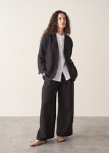 Woman wearing a black linen blazer, black wide leg linen trousers and a white top.