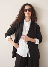 Woman wearing a black linen blazer, black wide leg linen trousers and a white top.