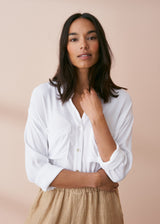Woman wearing a classic white crepe button up shirt with pocket details, styled with neutral trousers
