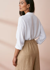 Woman wearing a white fluid button up shirt with pocket details, styled with a pair of neutral trousers