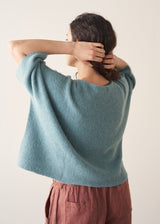 Woman wearing teal knitted sweater and rust red linen trousers