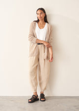 A woman wearing a soft knit cardigan in a light beige colour, worn over a white vest top and paired with matching beige trousers.