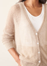 A woman wearing a soft knit cardigan in a light beige colour, worn over a white vest top and paired with matching beige trousers.