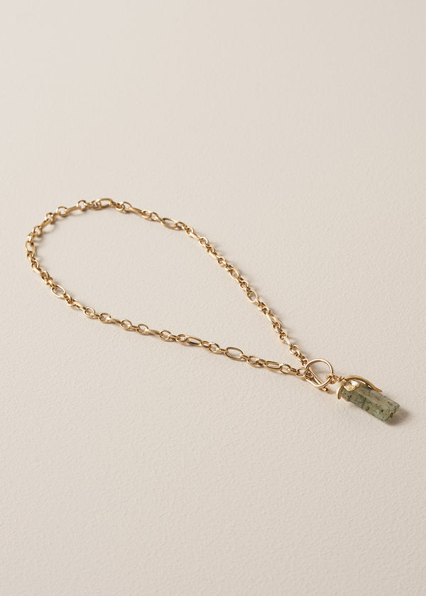 Gold chunky chain necklace with a green stone pendant on a beige background