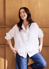 Woman wearing an oversized white linen shirt with blue denim jeans against a beige background