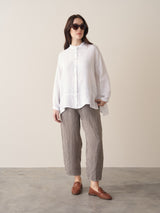 Woman wearing a white linen shirt and checked trousers with brown loafers, against a beige background