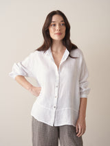 Woman wearing an oversized white linen shirt and checked trousers against a beige background