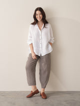 Woman wearing an oversized white linen shirt and checked trousers with brown loafers, against a beige background
