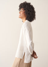 Woman wearing a white striped shirt and beige wide leg trousers against a plain background.