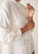 Woman wearing a white striped shirt and beige wide leg trousers against a plain background.