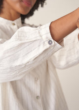 Woman wearing a white striped shirt and beige wide leg trousers against a plain background.