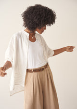Woman wearing a white striped shirt and beige wide leg trousers against a plain background.