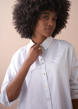 Woman wears a white boxy cotton shirt with gold ring