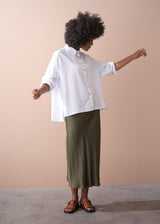 Woman wears white boxy cotton shirt with green satin skirt and brown sandals