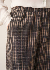 A woman wearing dark brown check barrel leg trousers with a white blouse and matching check jacket