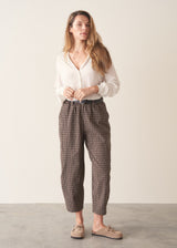 A woman wearing dark brown check barrel leg trousers with a white blouse and matching check jacket