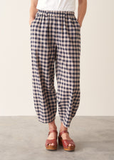 Woman wearing blue and taupe check barrel leg trousers with clog heels and a white t-shirt.