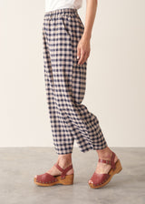 Woman wearing blue and taupe check barrel leg trousers with clog heels and a white t-shirt.