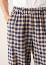 Woman wearing blue and taupe check barrel leg trousers with clog heels and a white t-shirt.