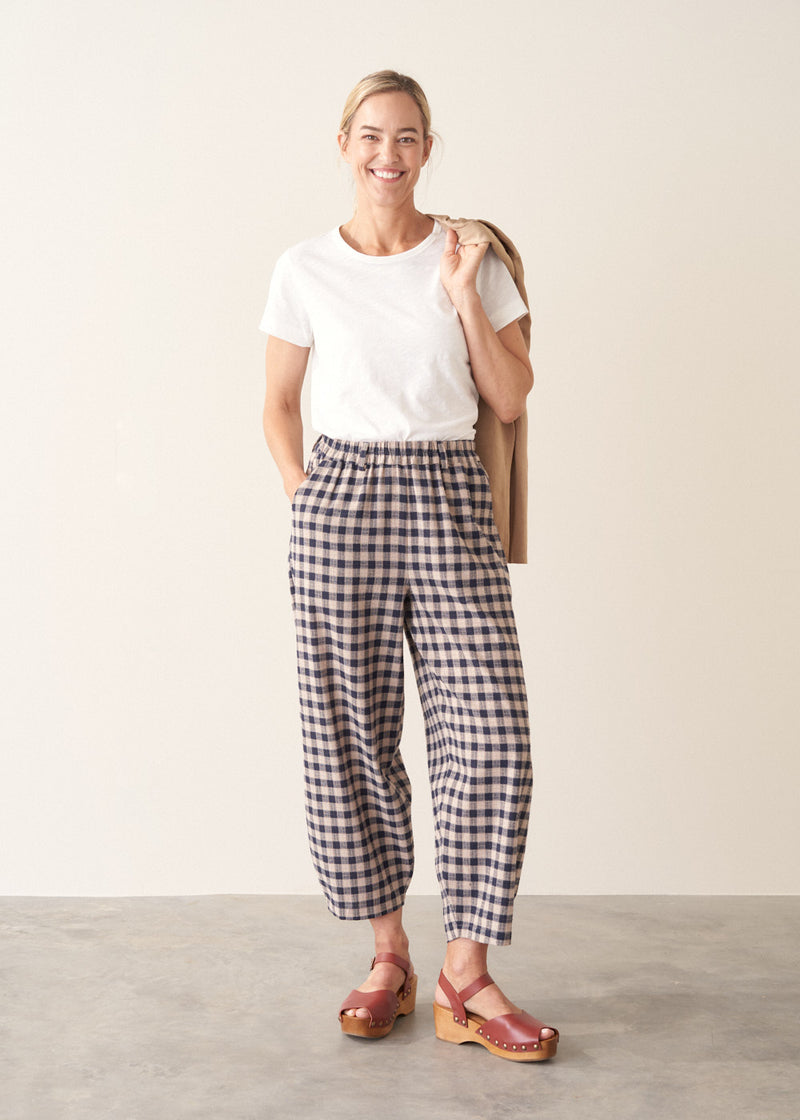 Woman wearing blue and taupe check barrel leg trousers with clog heels and a white t-shirt.