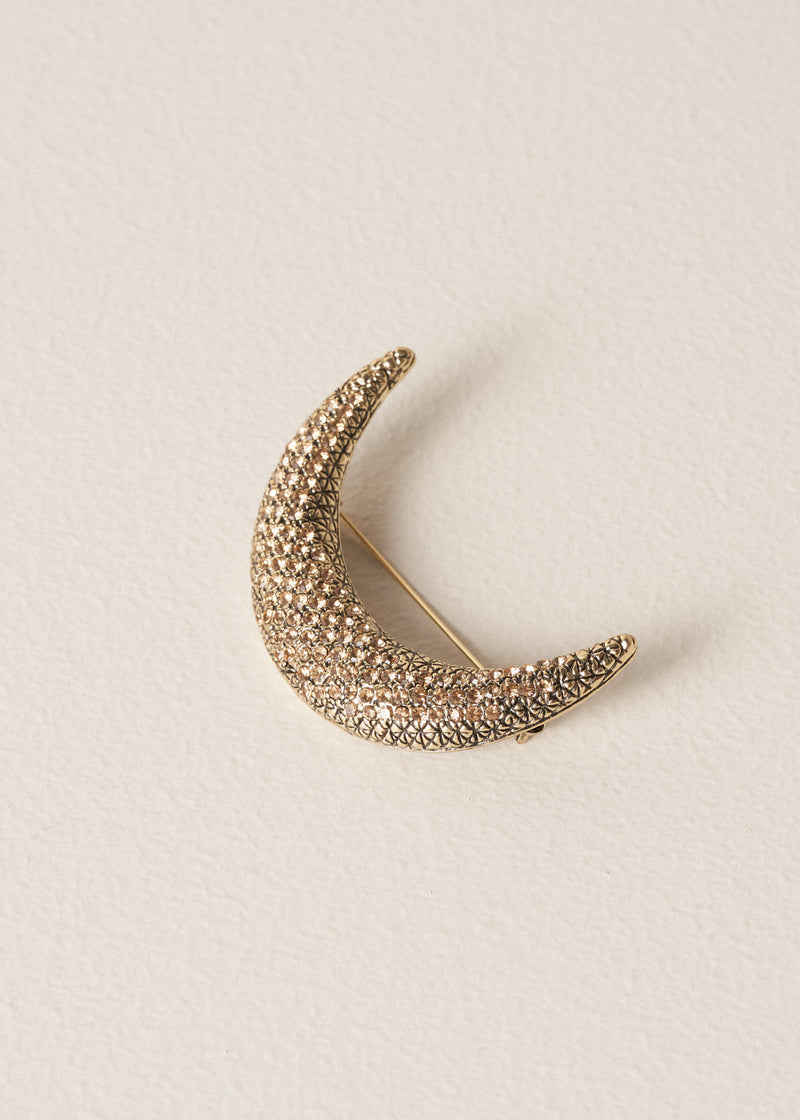 Gold crescent embellished moon brooch on a beige background