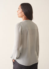 A woman wearing a light blue v-neck  blouse with dark jeans against a plain background