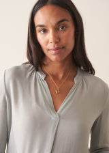 A woman wearing a light blue v-neck  blouse with dark jeans against a plain background