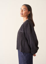 A woman wearing a black embroidered textured cropped jacket over a white top and dark blue jeans.