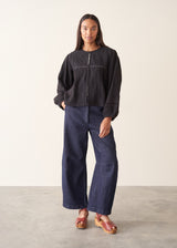 A woman wearing a black embroidered textured cropped jacket over a white top and dark blue jeans.