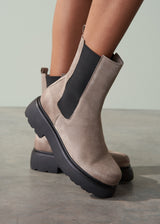 Brown suede Chelsea boots with black soles worn by a person on a neutral background