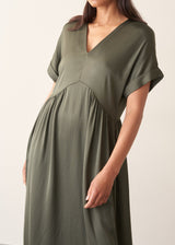 A woman wearing a loose, short-sleeve olive green satin maxi dress with a V-neckline