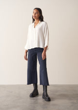 Woman wearing a white blouse and navy pants against a plain background