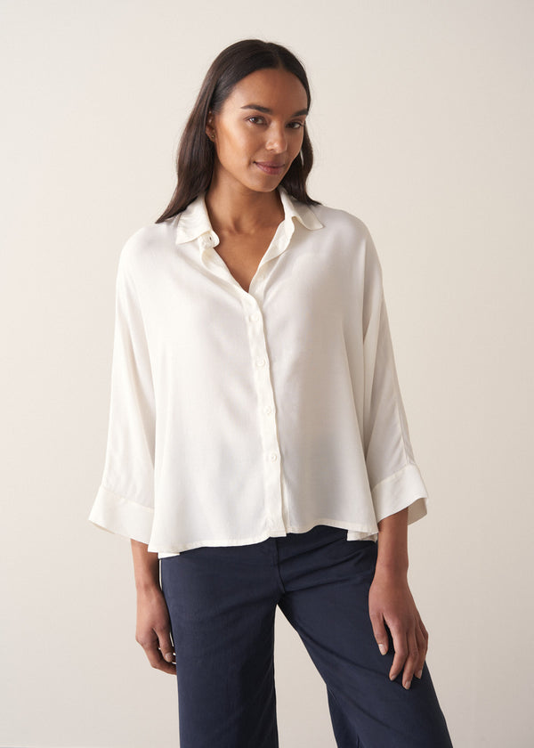 Woman wearing a white blouse and navy pants against a plain background