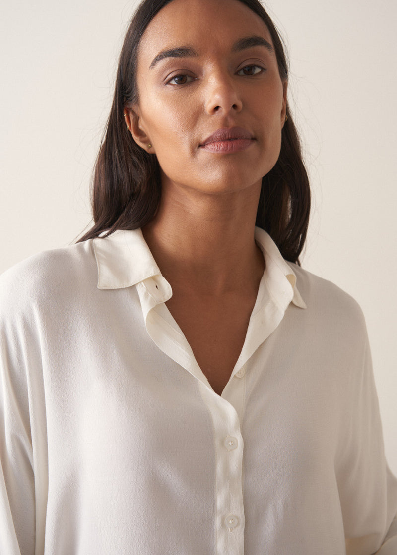 Woman wearing a white blouse and navy pants against a plain background
